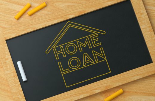 On a black slate the words 'Home Loan' is written and a home image is drawn. There are yellow and white chalk pieces around.