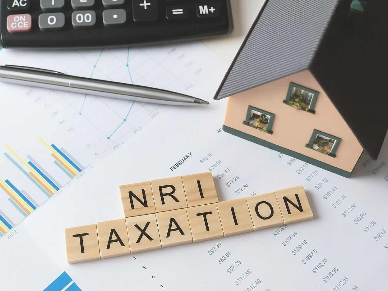 Miniature house placed on financial documents and graphs, alongside a calculator, pen, and wooden tiles spelling out “NRI TAXATION” representing property tax rules, financial planning, and compliance for NRIs investing in Indian real estate.